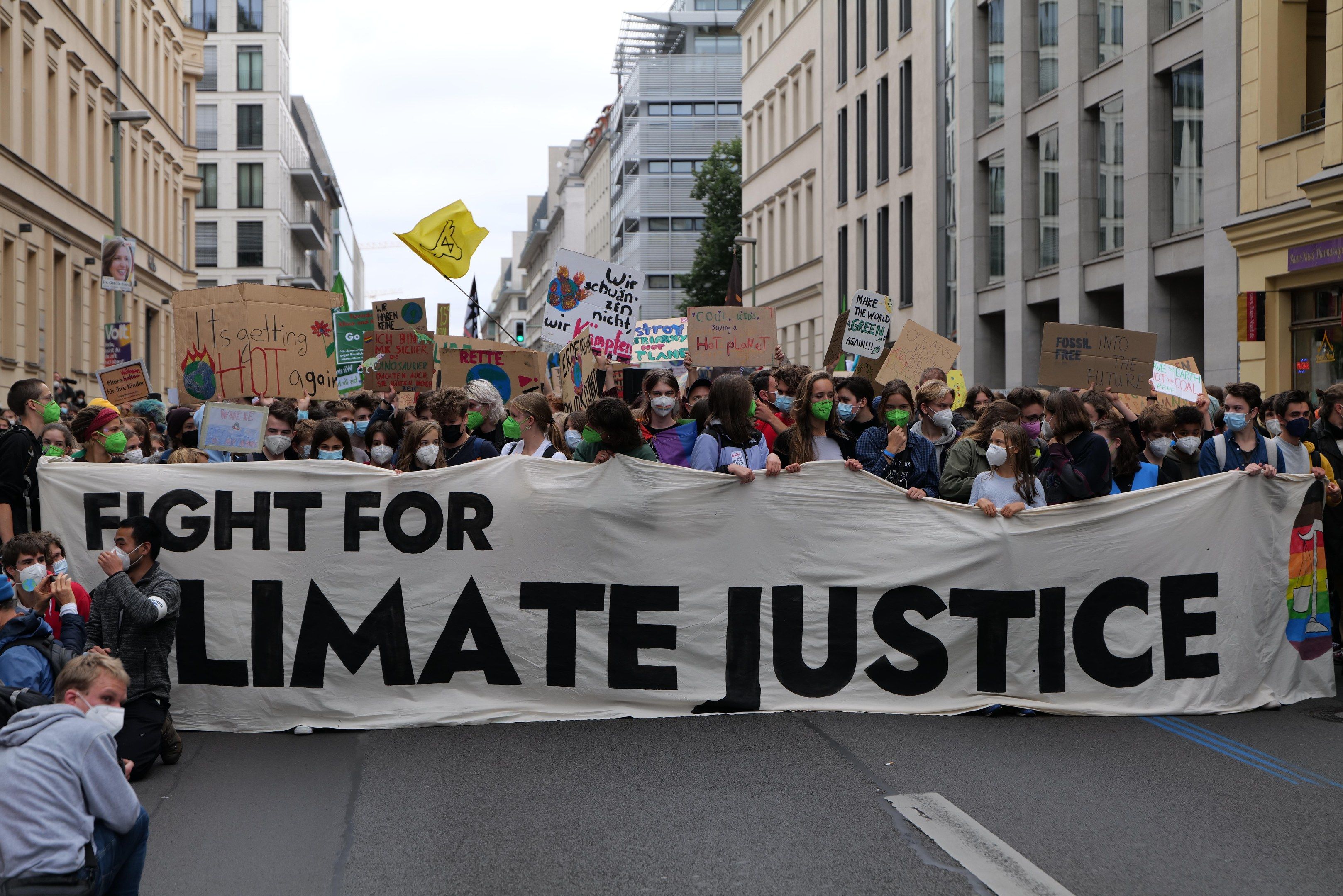 The image shows a group of people walking down a street, holding a banner that reads "Fight for...