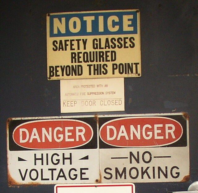 The image shows a notice board with three warning signs attached to the wall. The signs are...