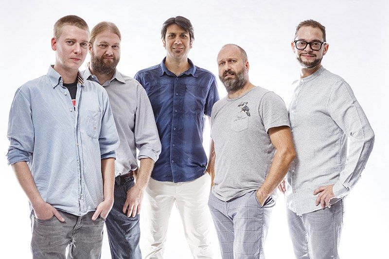 The image shows a group of men standing next to each other in front of a white background, with one...