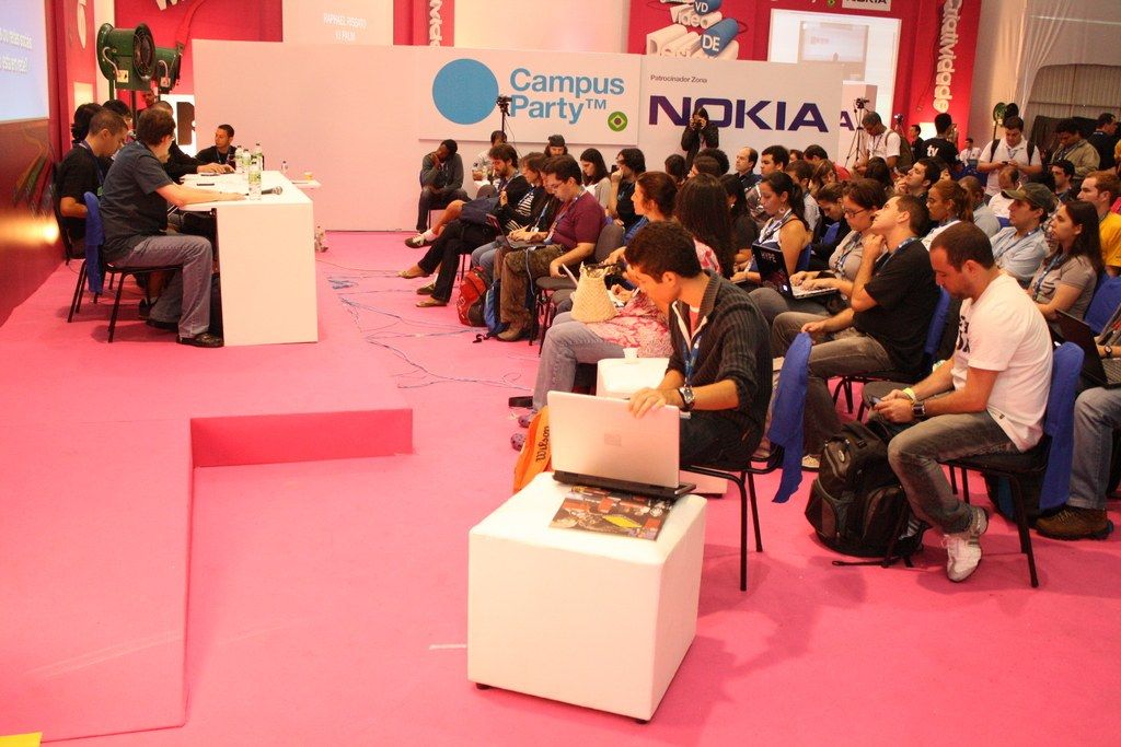 In this image there is a conference in which there are people sitting in chair and listening to the...