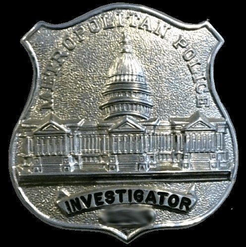 The image shows a silver police badge with the words "Investigator" written on it against a white...