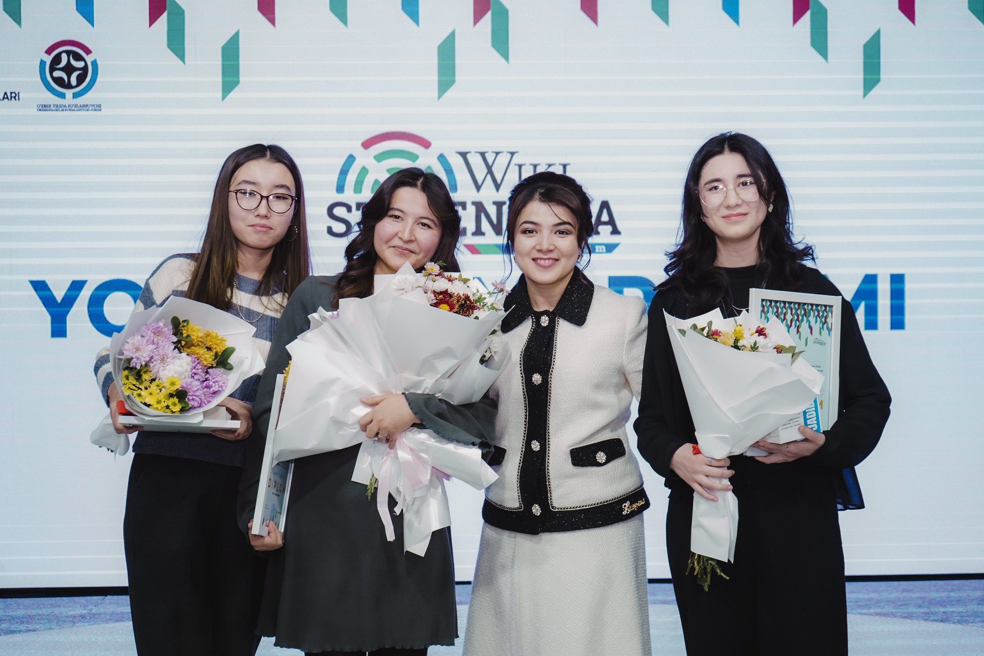 The image shows a group of four women standing next to each other, each holding a bouquet of...