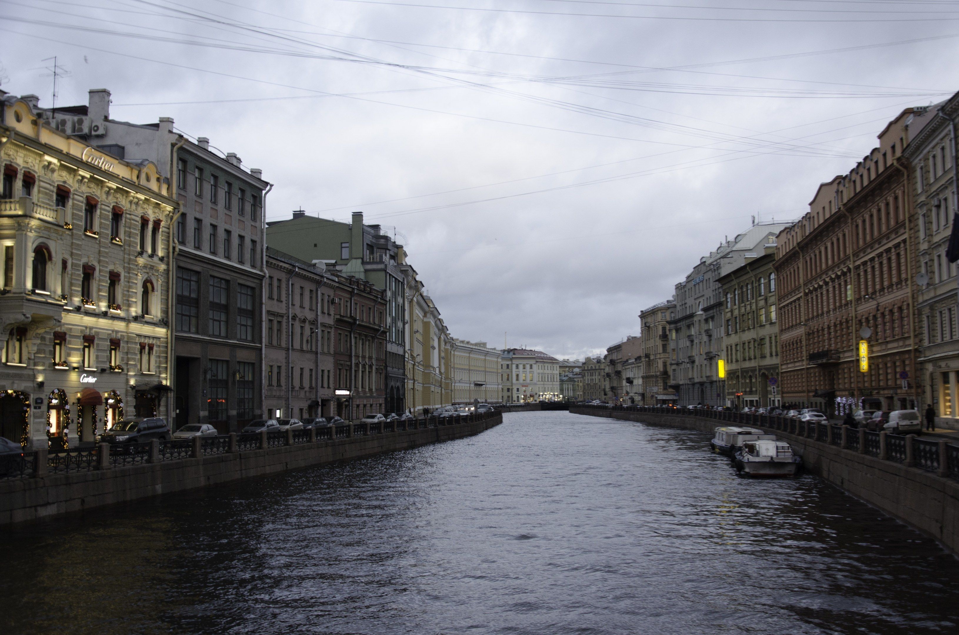 The image shows a canal in St. Petersburg, Russia, with boats on the water, a railing along the...