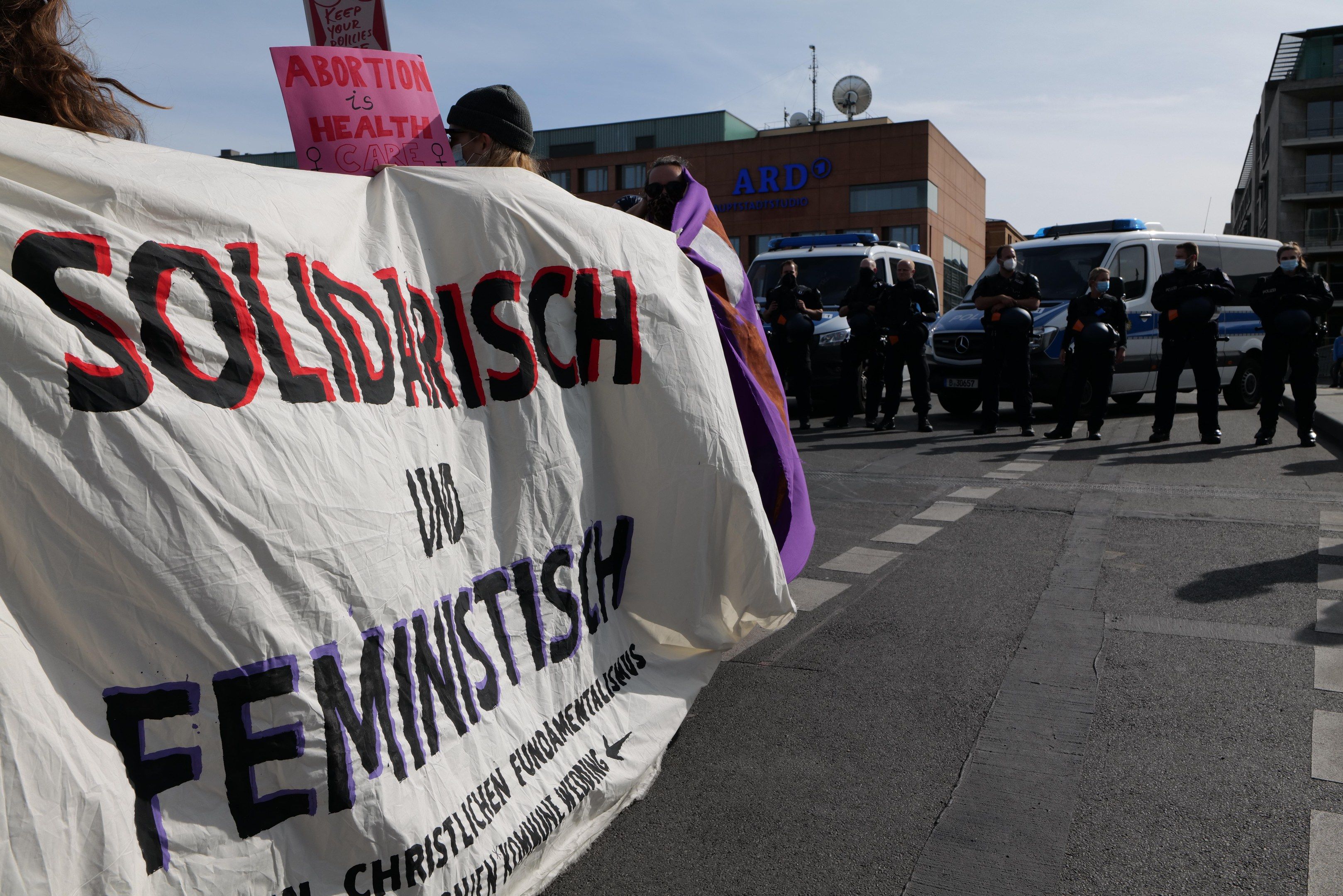 The image shows a group of people walking down a street, holding a banner that reads "Solidarity...