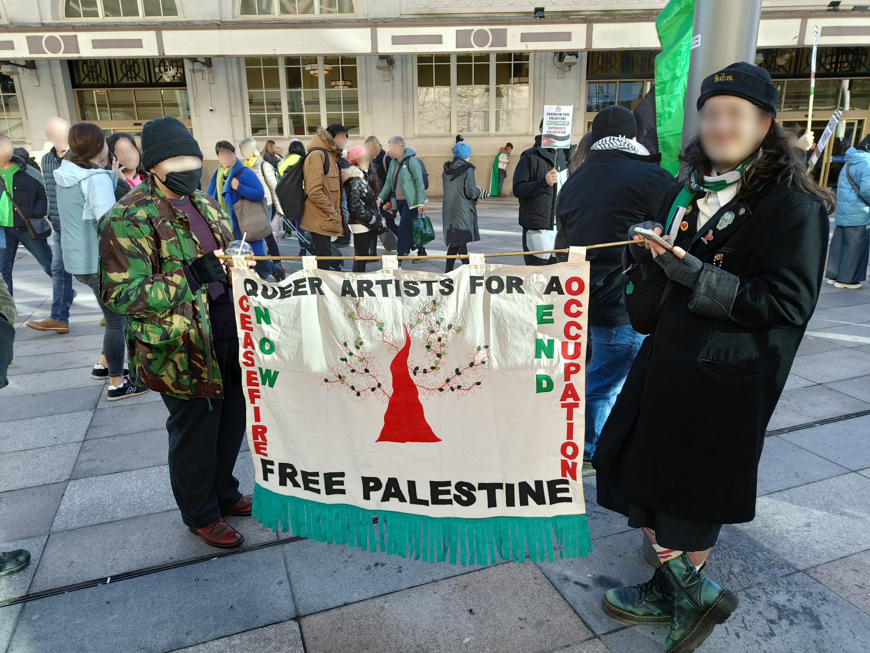 The image shows a group of people standing on the ground, some of them holding a banner that reads...