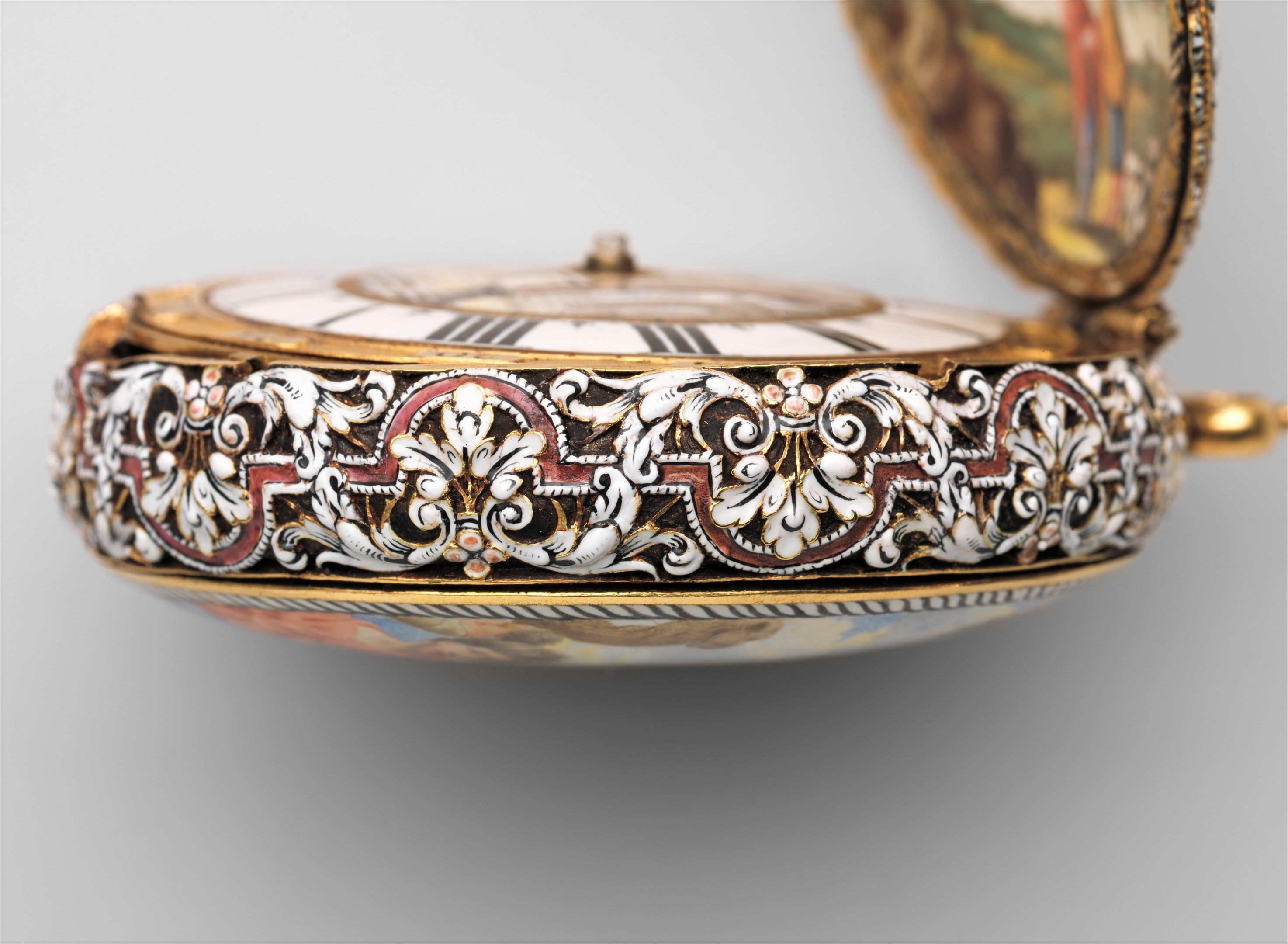 The image shows a close up of a pocket watch with a painting on it. The watch is encrusted with...