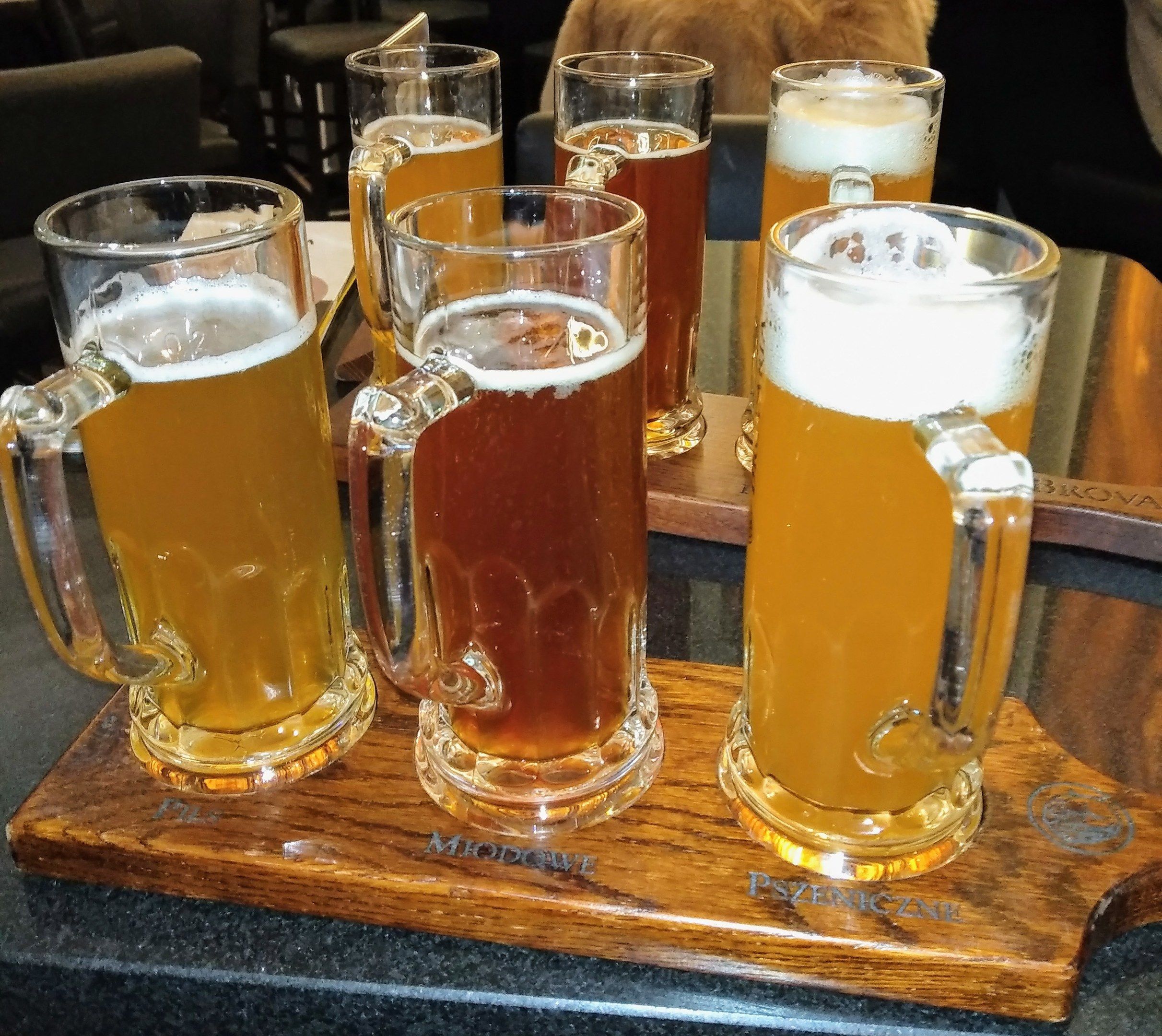 The image shows a wooden tray with four mugs of beer sitting on top of it. In the background, there...