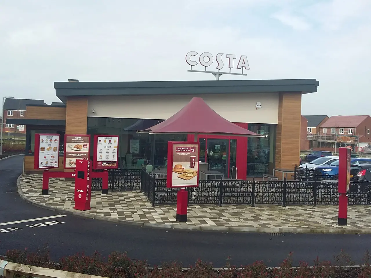 The image shows a Costa restaurant with cars parked in front of it, surrounded by buildings, street...