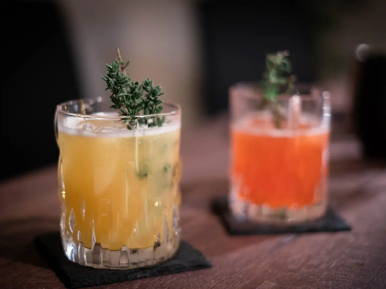 The image shows two glasses filled with different types of drinks on top of a wooden table, with a...