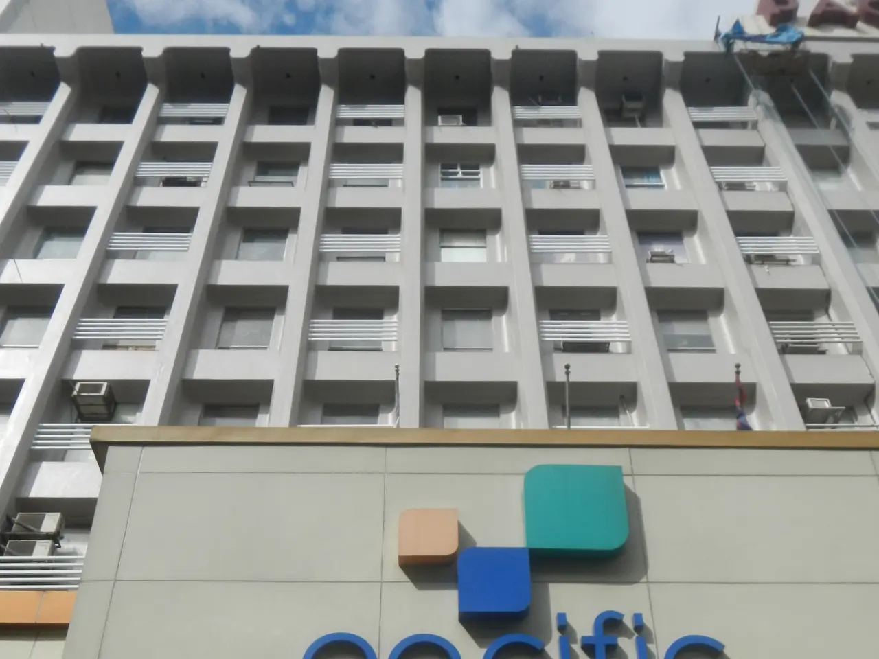 The image shows the Pacific Centre Hotel in Bangkok, Thailand. It is a building with windows, air...