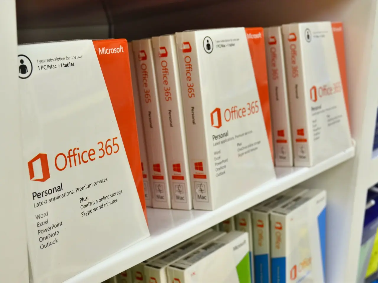 The image shows a shelf filled with boxes of Microsoft Office 365 on top of a white shelf. The...