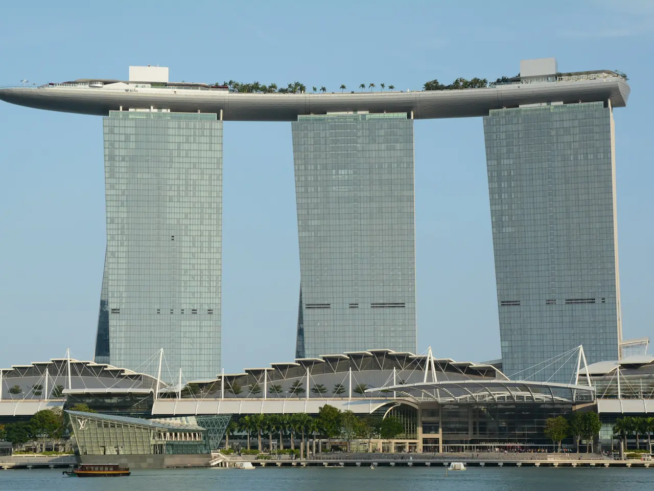 The image shows the iconic Marina Bay Sands Hotel in Singapore, with its towering skyscrapers, lush...
