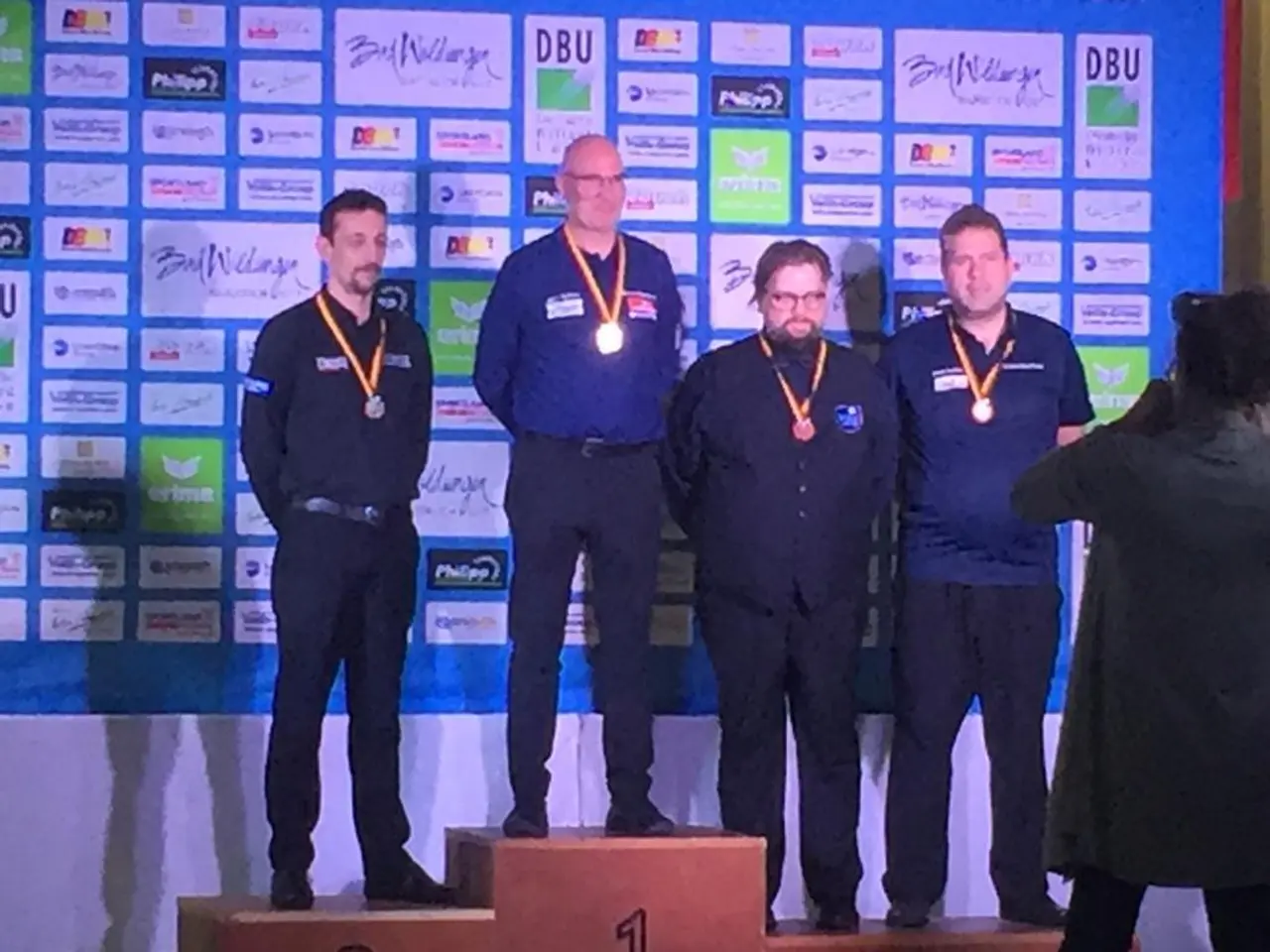 The image shows a group of five men standing on top of a podium, wearing medals around their necks....