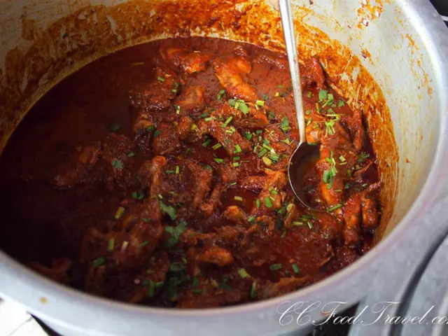 There is a meat curry and an object in the vessel. In the bottom right, there is a watermark.