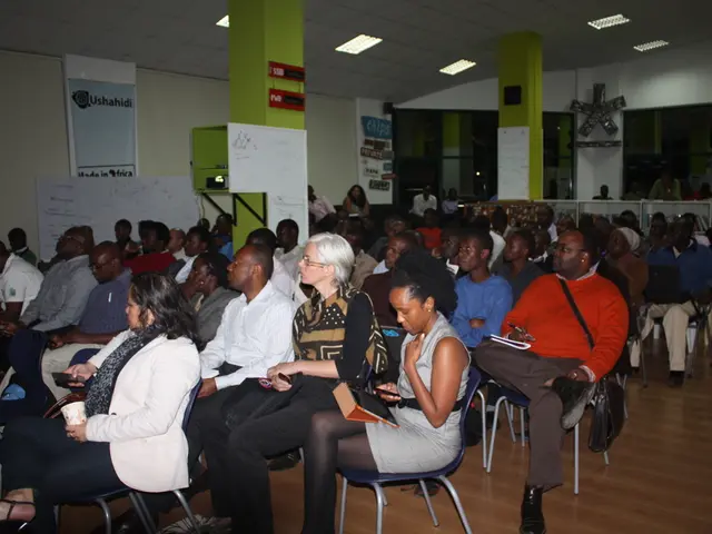 It looks like a classroom,there are many people sitting on the chairs there are two green color...