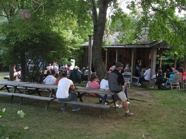 As we can see in the image there are few people here and there, a house, benches, chairs, grass and...