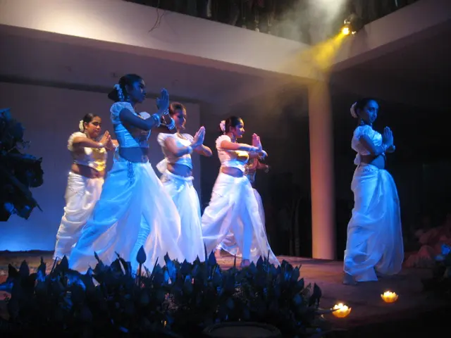 In this image a group of people are dancing ,In front of stage a group of plants are placed and...