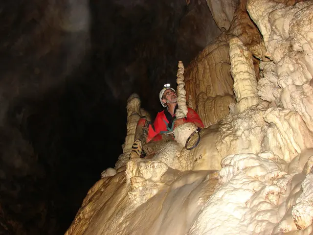In this image there is a person sitting inside a cave.