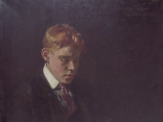 The image shows a young boy sitting at a table, engrossed in a book he is holding in his hands. He...