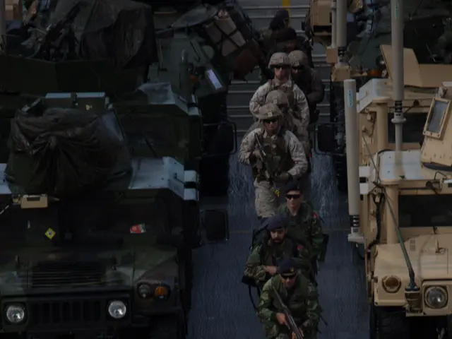 The image shows a group of soldiers wearing helmets and holding guns, walking across a bridge with...
