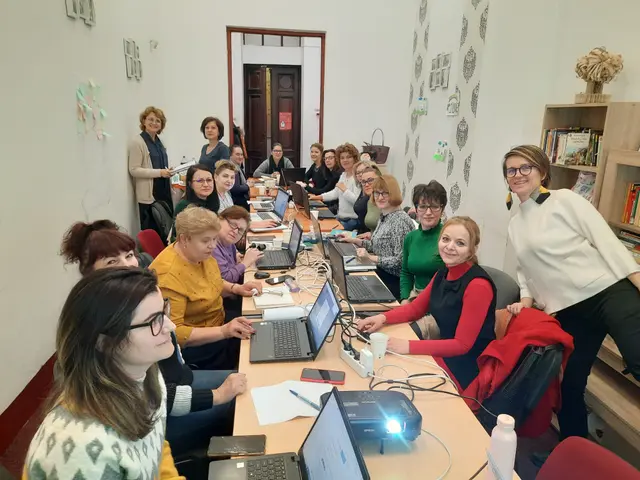 The image shows a group of women sitting around a table with laptops, wires, a projector, a bottle,...