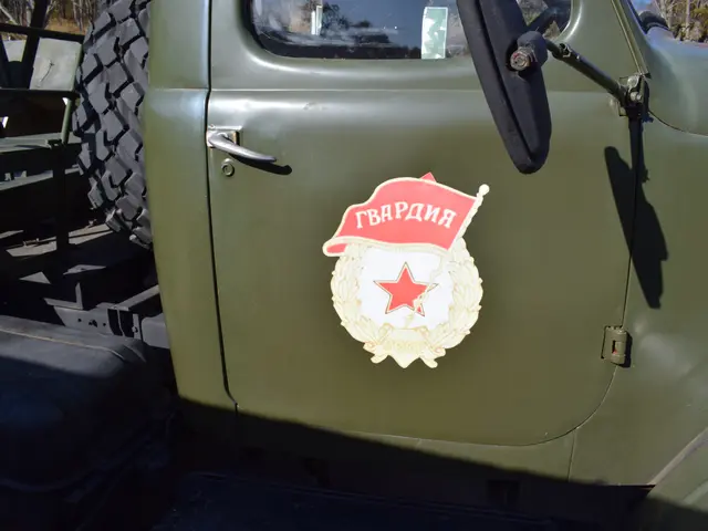 The image shows an old military truck with a badge on the side of it, parked in front of a backdrop...