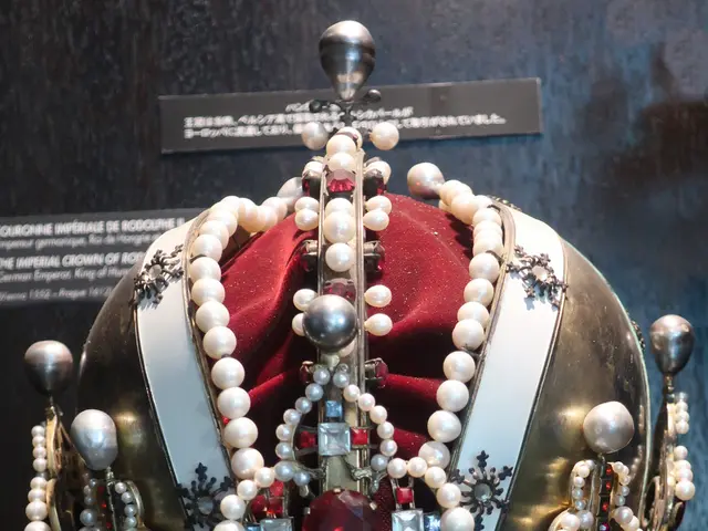 The image shows a gold crown with pearls and jewels on display in a museum, with a board in the...