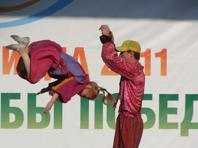 The image shows a man and a woman performing acrobatics on a stage, surrounded by mics with stands,...
