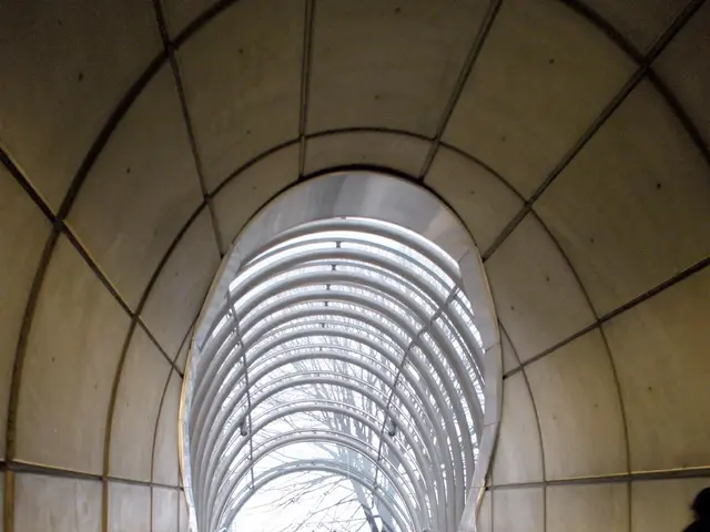 The image shows an escalator in a subway station with people on it, surrounded by walls on either...
