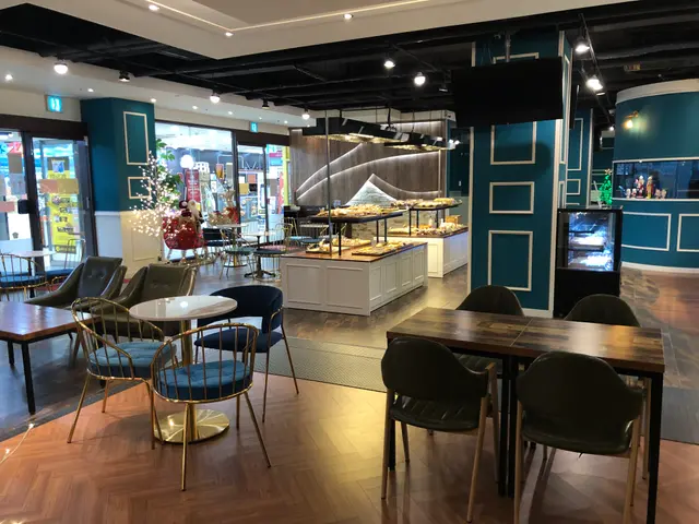 The image shows a restaurant with tables and chairs in front of a large window, illuminated by...