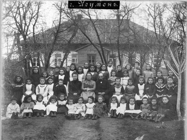 The image shows a black and white photo of a group of children posing for a picture in front of a...