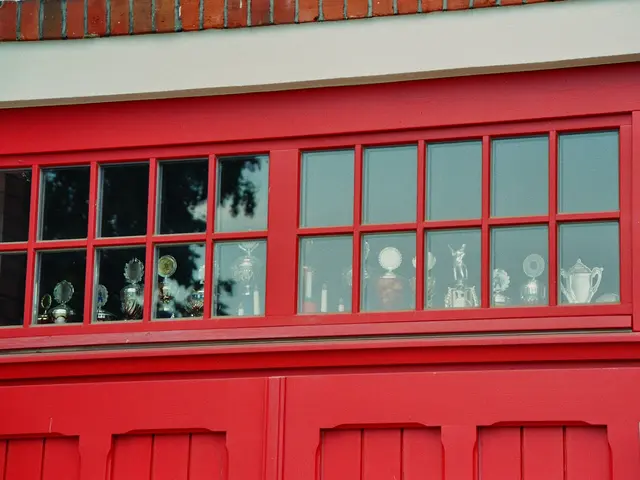 The image shows a red fire station with a red door and glass windows, through which trophies can be...
