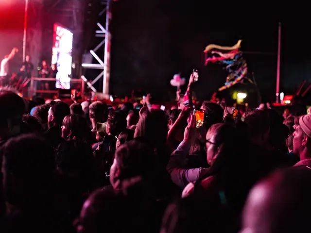 The image shows a crowd of people at a concert with their hands in the air, some of them holding...