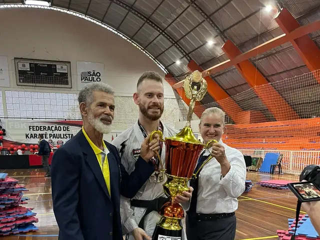 The image shows three men standing next to each other, proudly holding a trophy. On the right side...