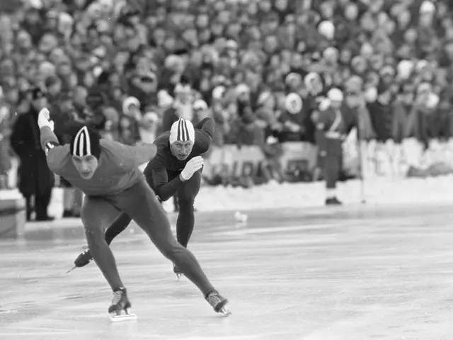 The image shows two men speed skating on an ice rink in front of a large crowd. They are both...
