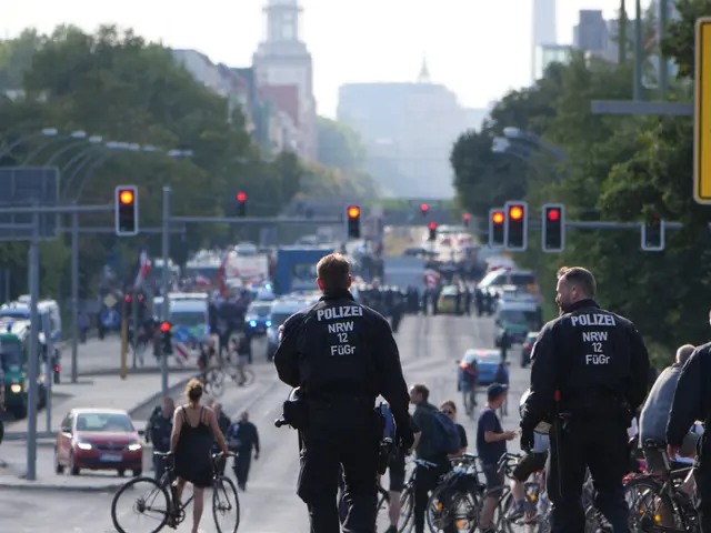 The image shows a group of police officers riding bicycles down a street lined with trees, poles,...