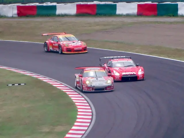 The image shows three sports cars racing on a race track, with grass on either side of the track...