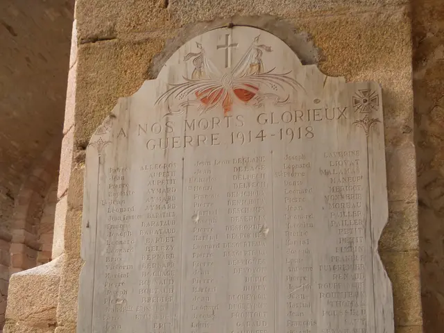 The image shows a stone plaque on the side of a stone building, with text inscribed on it. The...