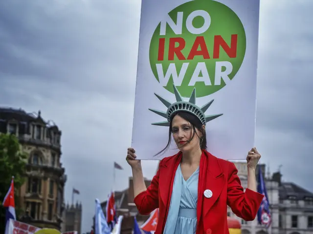 The image shows a woman standing in the center, holding a sign that reads "No Iran War" with a...