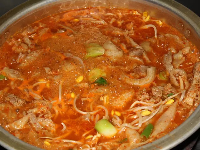 The image shows a pot filled with a hot pot of soup on top of a table. The pot is filled with...