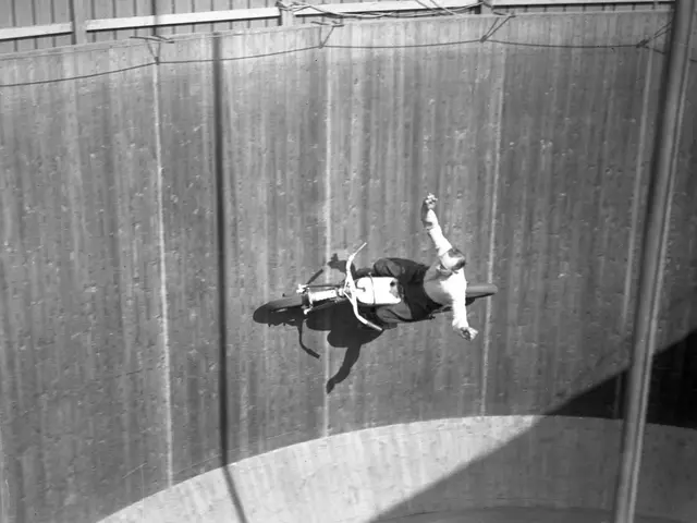 The image shows a man on a motorcycle doing a trick in the air, with a wall in the background and a...