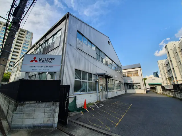 The image shows a Mitsubishi electric factory in Tokyo, Japan. It is a building with glass windows...