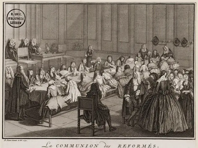 The image shows a group of people sitting around a table in a room, with some standing on the...