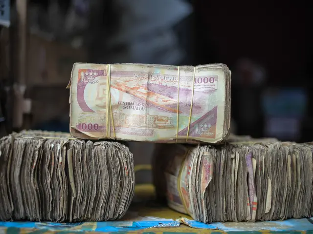 The image shows a pile of money sitting on top of a table, with a blurred background. The money...