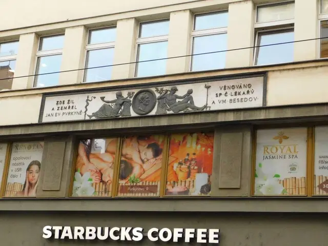 The image shows a Starbucks coffee shop in Prague, Czech Republic. The building has glass windows...
