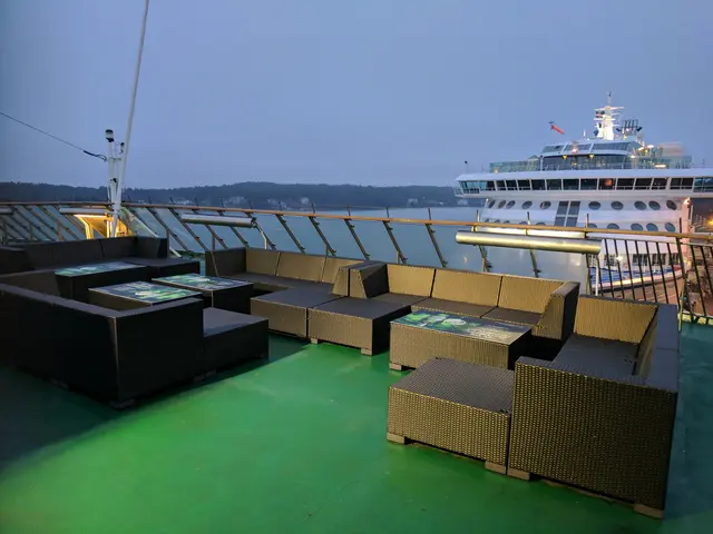 The image shows a large cruise ship docked in the water at night, with sofas and tables on the...