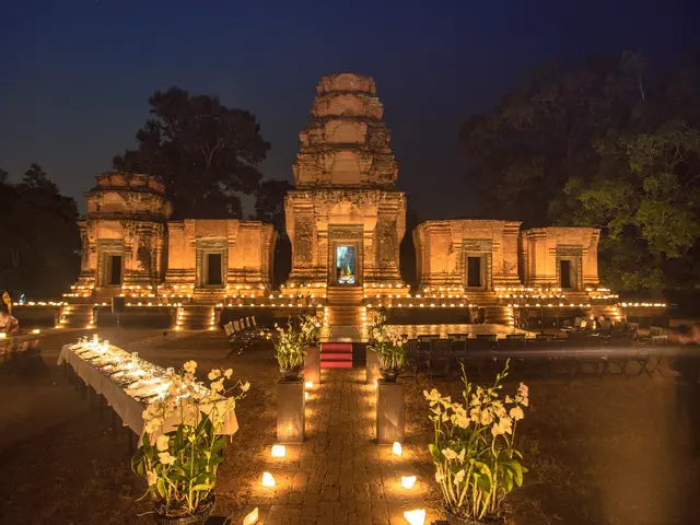 The image shows a group of people standing in front of a temple at night, illuminated by lights and...