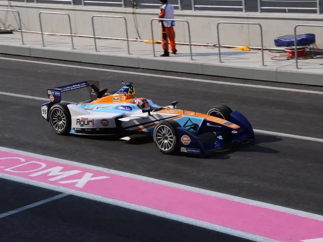 The image shows a man driving a Formula car on a race track, with a person wearing a helmet in the...