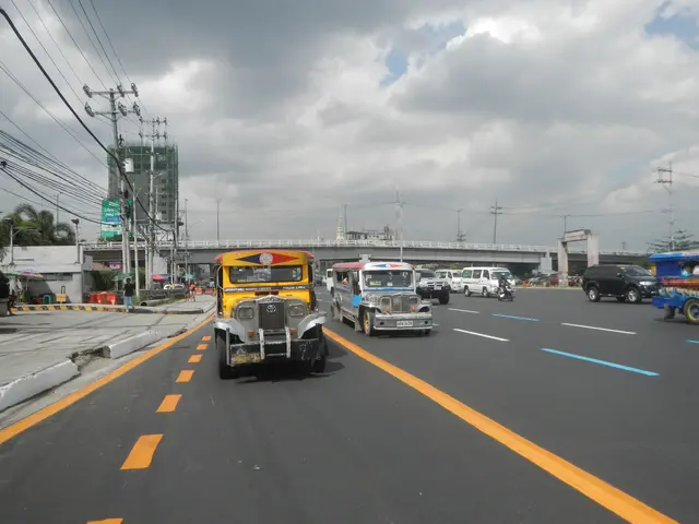 The image shows a busy street with a variety of vehicles, including a jeepney, driving down it. On...