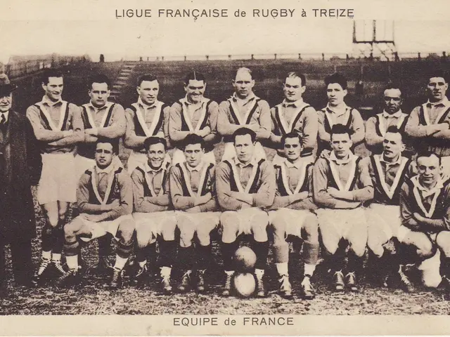 The image shows an old black and white photo of a rugby team, with a few people standing and a few...